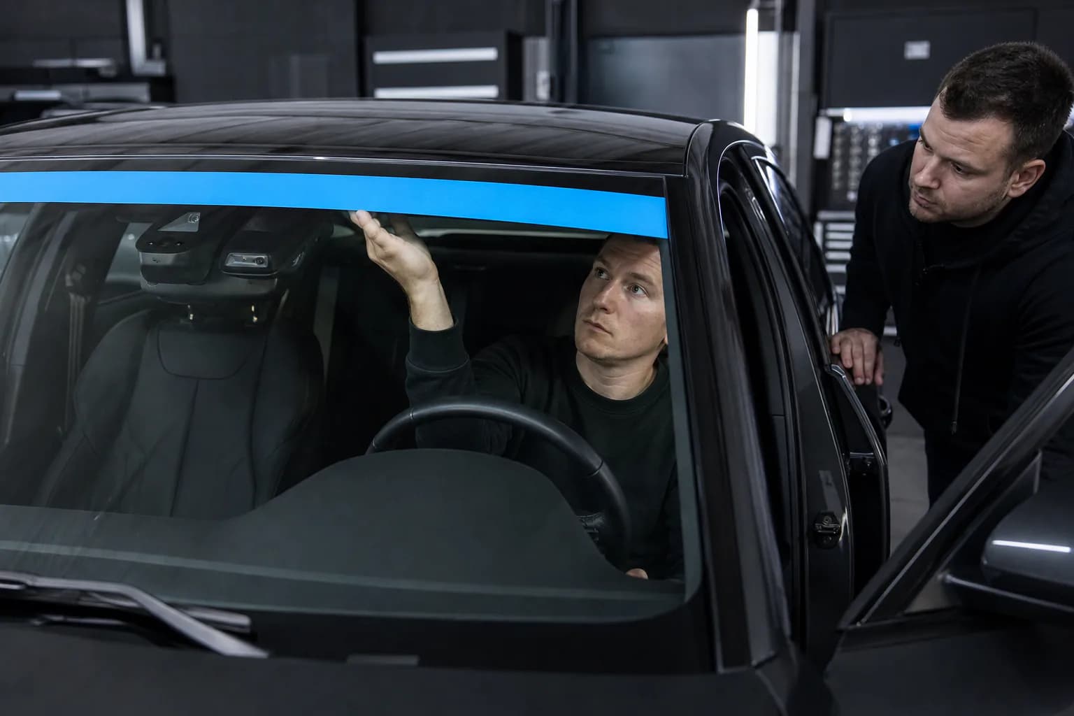 Due tecnici verificano una fascia adesiva azzurra sulla parte alta del parabrezza
